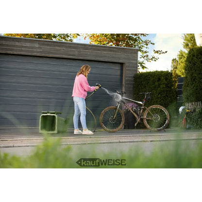 Frau in pinkem Pullover und Jeans mit Kärcher WBS 3 Reinigungspistole auf schmutzigem Mountainbike